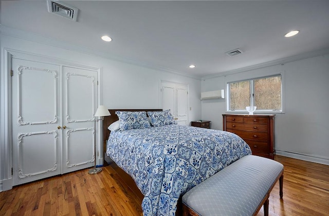 bedroom with a wall mounted AC, wood-type flooring, and ornamental molding