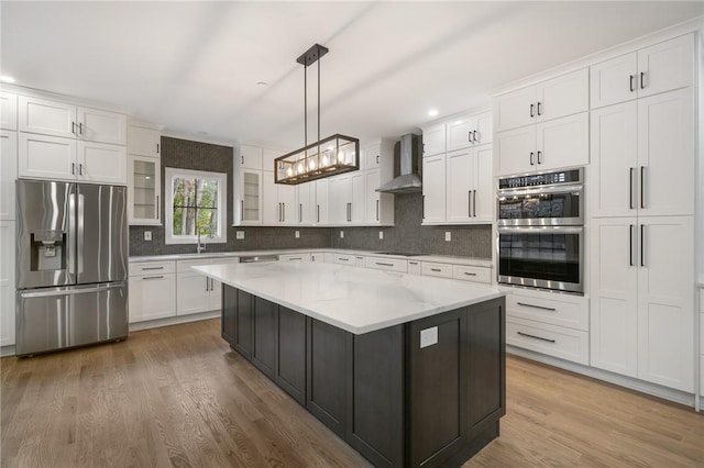 kitchen with stainless steel appliances, white cabinetry, wall chimney range hood, a center island, and pendant lighting