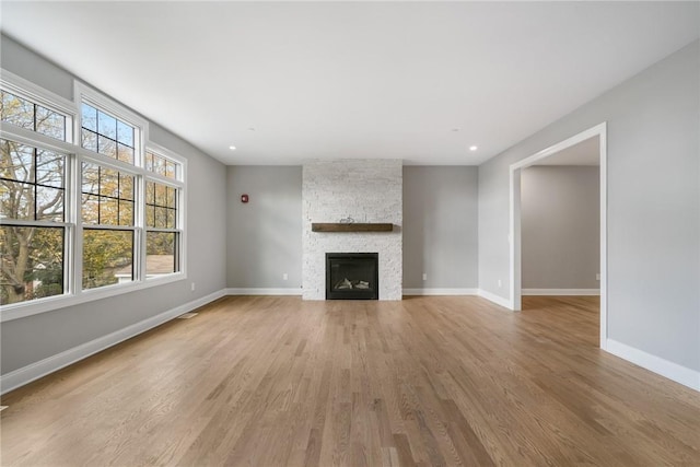 unfurnished living room with recessed lighting, light wood-style flooring, baseboards, and a stone fireplace