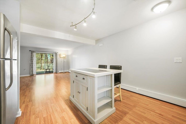 kitchen featuring stainless steel fridge, light wood-type flooring, baseboard heating, a kitchen island, and a kitchen bar