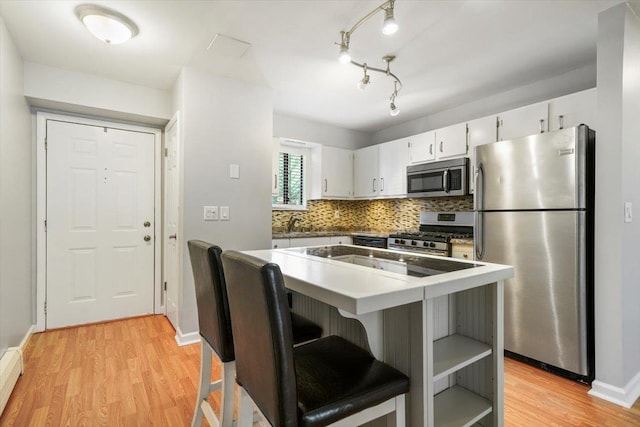 kitchen with a kitchen bar, white cabinets, stainless steel appliances, and light wood-type flooring