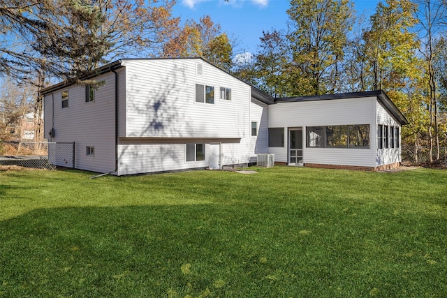 rear view of house with a sunroom, a lawn, and central AC