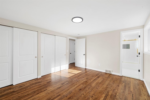 unfurnished bedroom featuring wood-type flooring and multiple closets