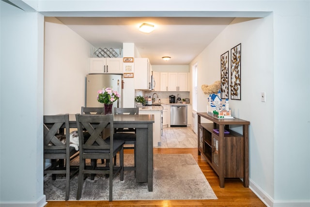 kitchen with white cabinets, sink, light wood-type flooring, tasteful backsplash, and stainless steel appliances