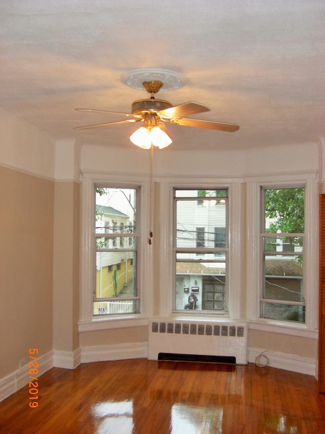 unfurnished room featuring ceiling fan, radiator heating unit, and wood-type flooring