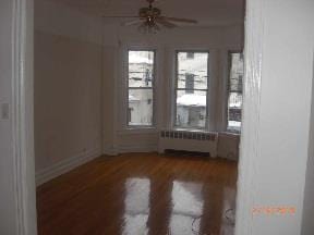 empty room featuring hardwood / wood-style flooring, ceiling fan, and radiator