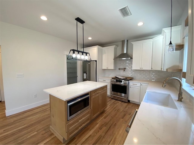 kitchen featuring stainless steel appliances, a sink, white cabinetry, wall chimney range hood, and a center island