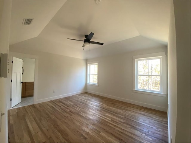 empty room featuring visible vents, vaulted ceiling, and baseboards