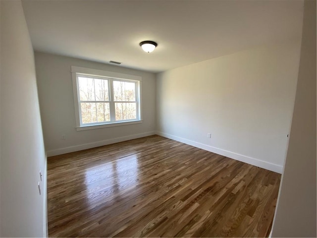 empty room featuring dark wood-type flooring, visible vents, and baseboards