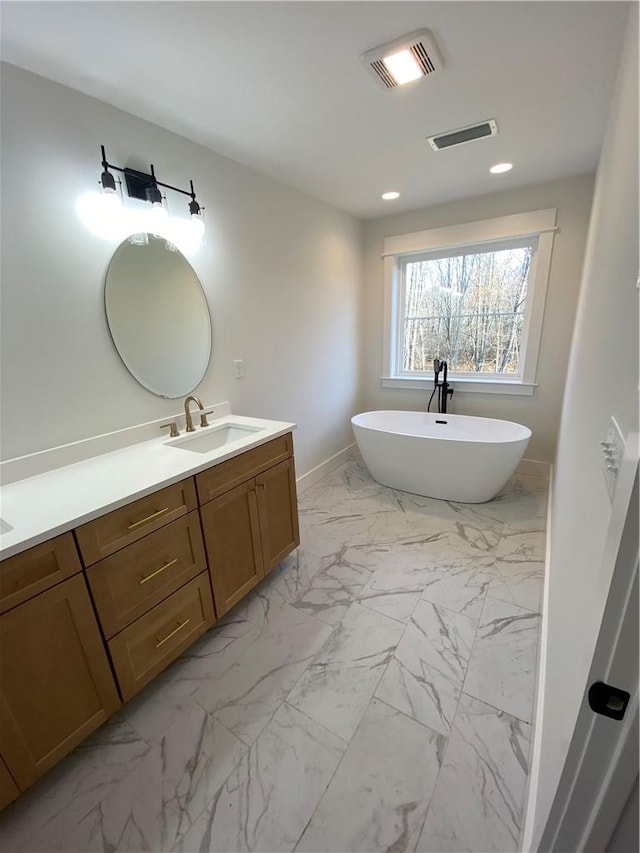 full bathroom with marble finish floor, double vanity, visible vents, a freestanding bath, and a sink