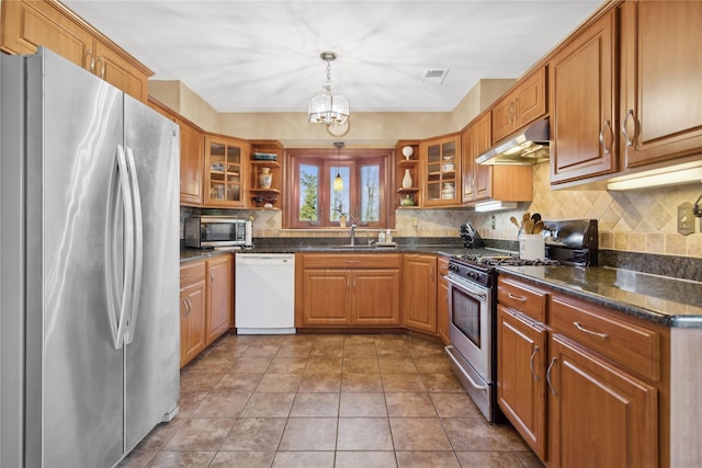 kitchen with sink, hanging light fixtures, stainless steel appliances, tasteful backsplash, and dark stone counters