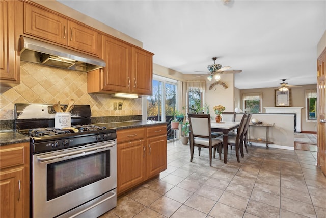 kitchen featuring backsplash, ceiling fan, dark stone countertops, light tile patterned floors, and stainless steel range with gas stovetop