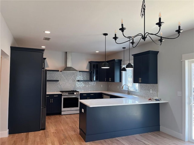 kitchen featuring wall chimney range hood, hanging light fixtures, light hardwood / wood-style flooring, gas stove, and kitchen peninsula