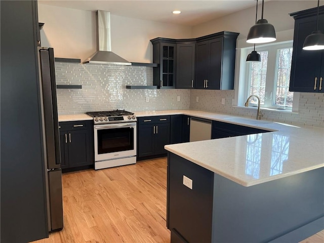 kitchen featuring sink, stainless steel appliances, wall chimney range hood, kitchen peninsula, and decorative light fixtures