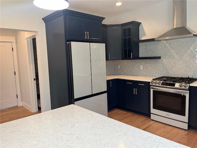 kitchen with wall chimney range hood, blue cabinets, fridge, light hardwood / wood-style floors, and gas stove