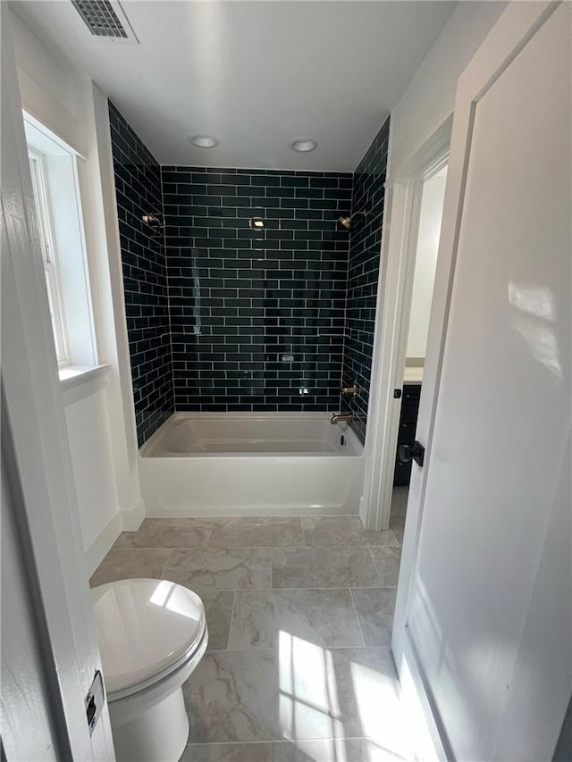 bathroom featuring tiled shower / bath combo and toilet