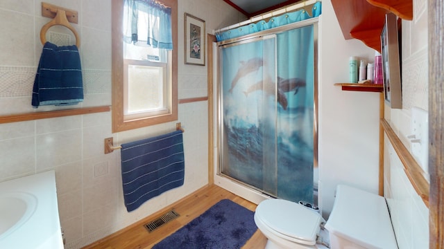 bathroom featuring walk in shower, hardwood / wood-style flooring, toilet, and tile walls