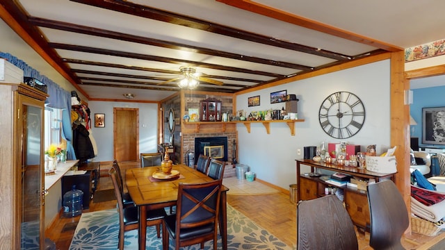 dining space featuring ceiling fan, beamed ceiling, light parquet floors, and a brick fireplace