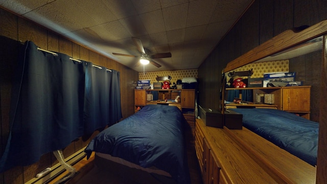 bedroom featuring ceiling fan, wooden walls, and a baseboard radiator