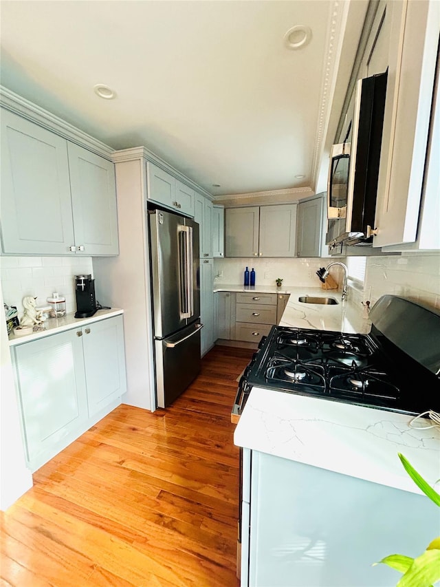 kitchen featuring decorative backsplash, appliances with stainless steel finishes, light stone countertops, sink, and light hardwood / wood-style floors