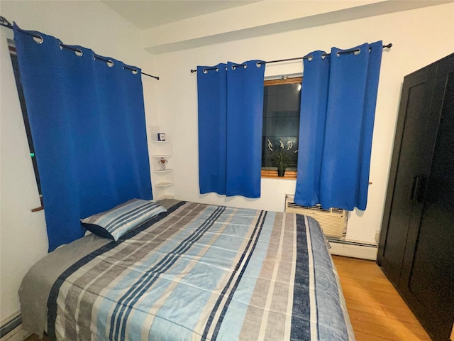 bedroom with a baseboard heating unit, wood finished floors, and a wall unit AC