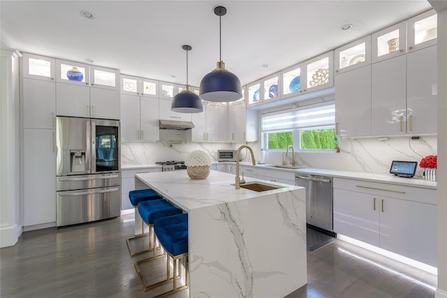 kitchen with dark wood-type flooring, decorative light fixtures, a center island with sink, white cabinets, and appliances with stainless steel finishes