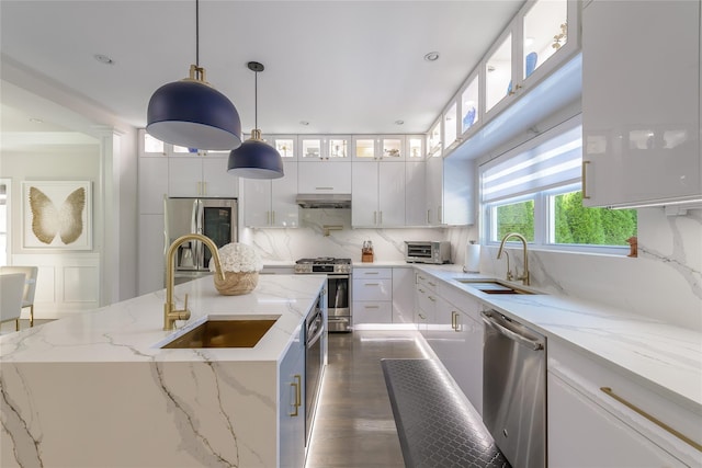 kitchen with stainless steel appliances, sink, decorative light fixtures, white cabinetry, and an island with sink