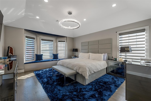 bedroom with hardwood / wood-style flooring, an inviting chandelier, lofted ceiling, and multiple windows