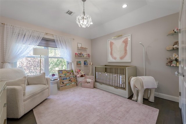 bedroom with dark hardwood / wood-style floors, a chandelier, and a nursery area