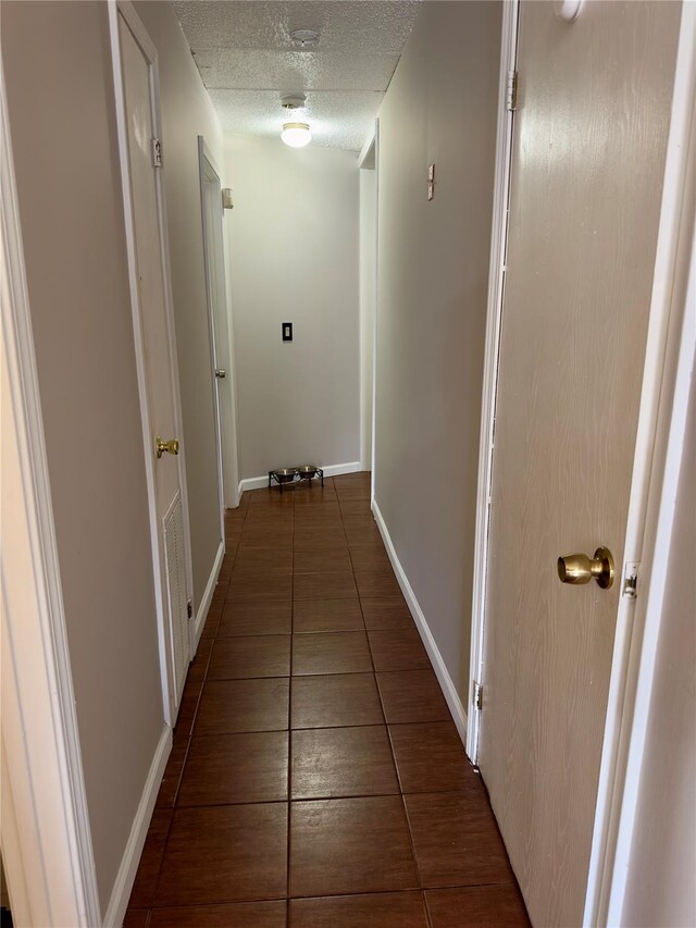 hallway featuring dark tile patterned floors and a textured ceiling