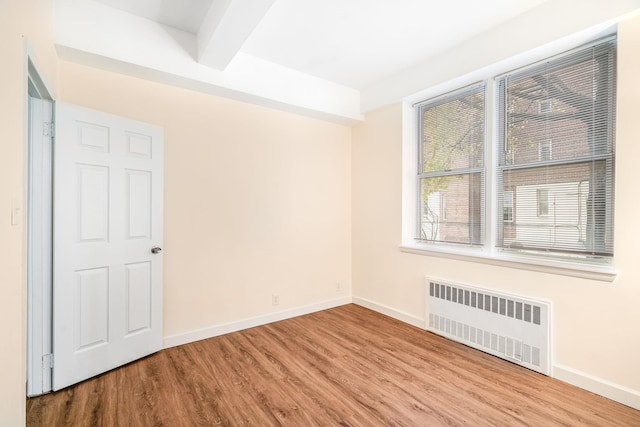 spare room with beamed ceiling, light wood-type flooring, and radiator