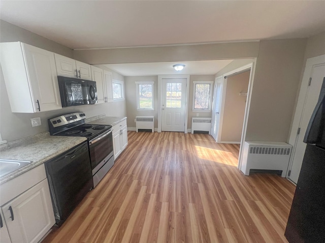 kitchen with black appliances, white cabinetry, and radiator heating unit