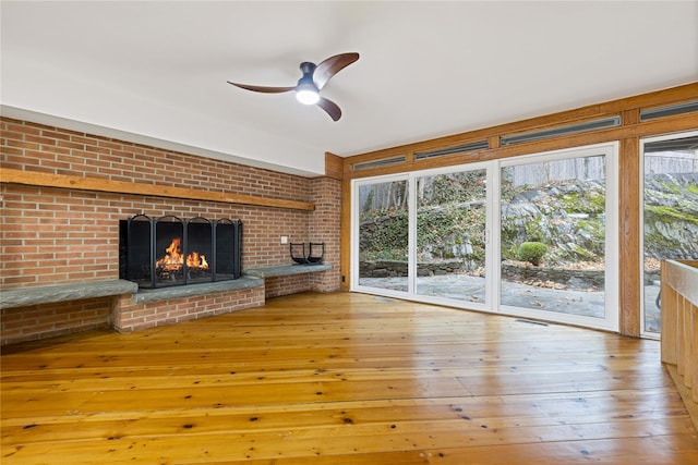 unfurnished living room featuring a wealth of natural light, hardwood / wood-style floors, ceiling fan, and a brick fireplace