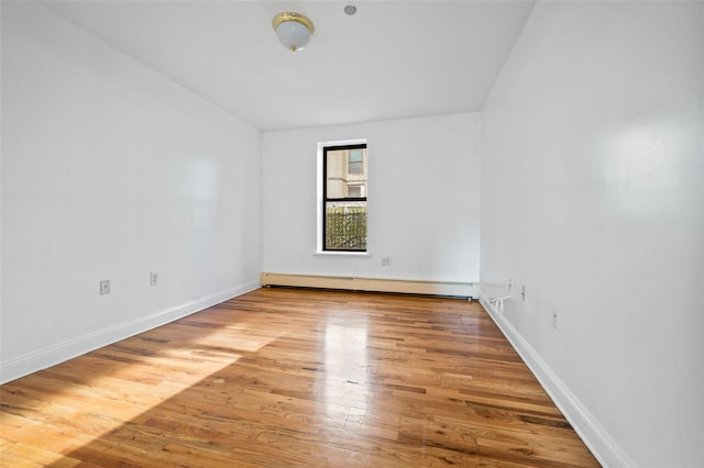 unfurnished room featuring hardwood / wood-style floors, vaulted ceiling, and a baseboard heating unit