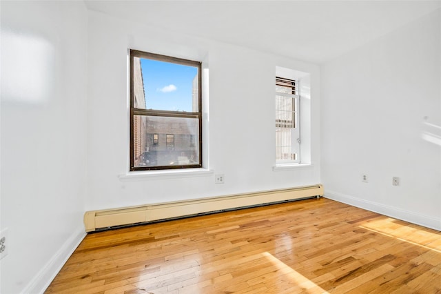 empty room featuring plenty of natural light, wood-type flooring, and baseboard heating