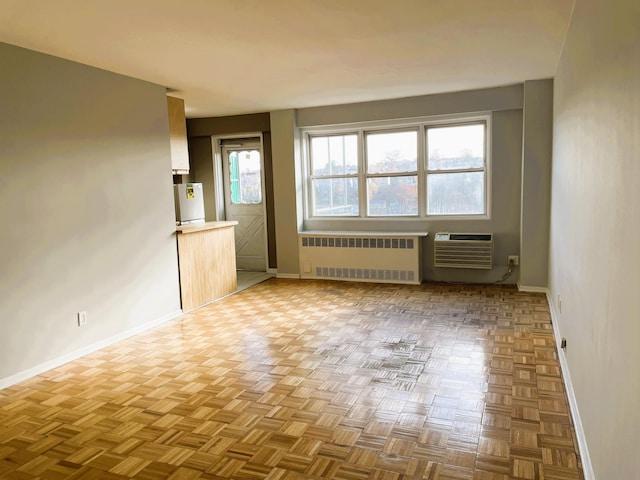 unfurnished living room featuring radiator heating unit, a wealth of natural light, and light parquet flooring