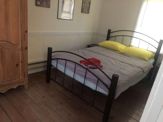 bedroom with wood-type flooring and a baseboard heating unit