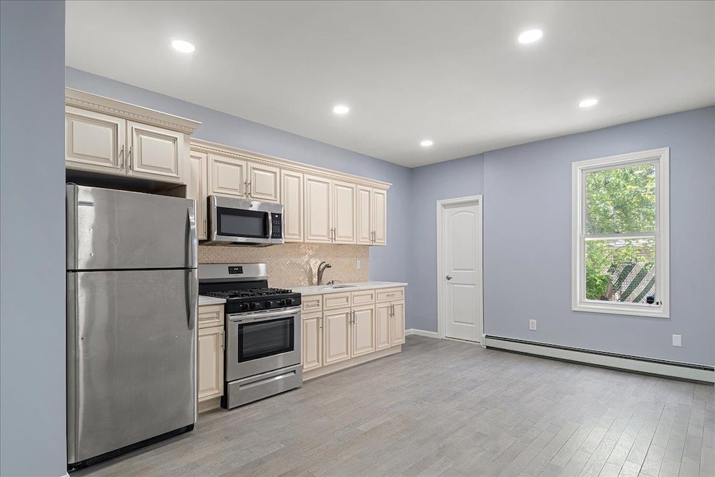 kitchen with cream cabinets, light hardwood / wood-style floors, a baseboard heating unit, and appliances with stainless steel finishes