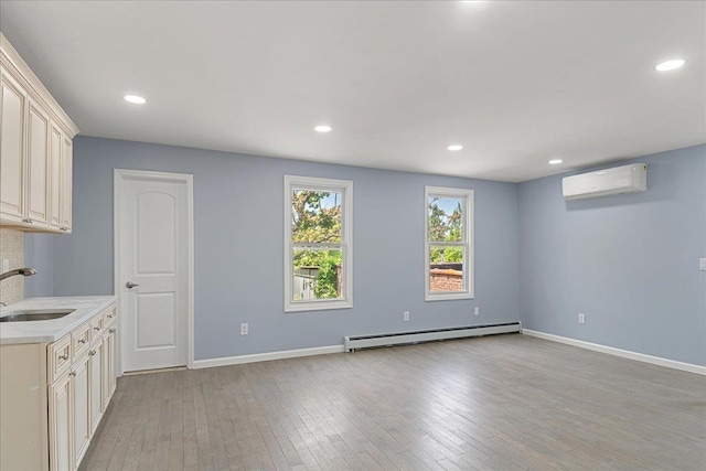 interior space with sink, baseboard heating, a wall mounted AC, cream cabinetry, and light hardwood / wood-style floors