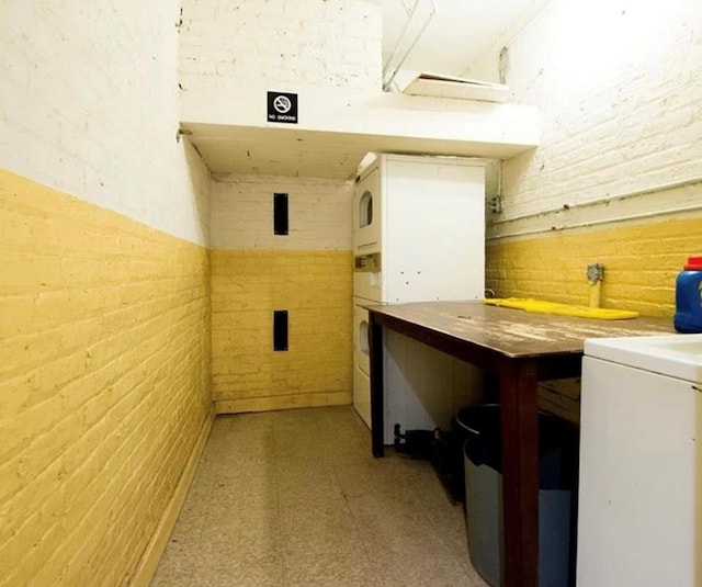 washroom with a workshop area, stacked washer and clothes dryer, and brick wall