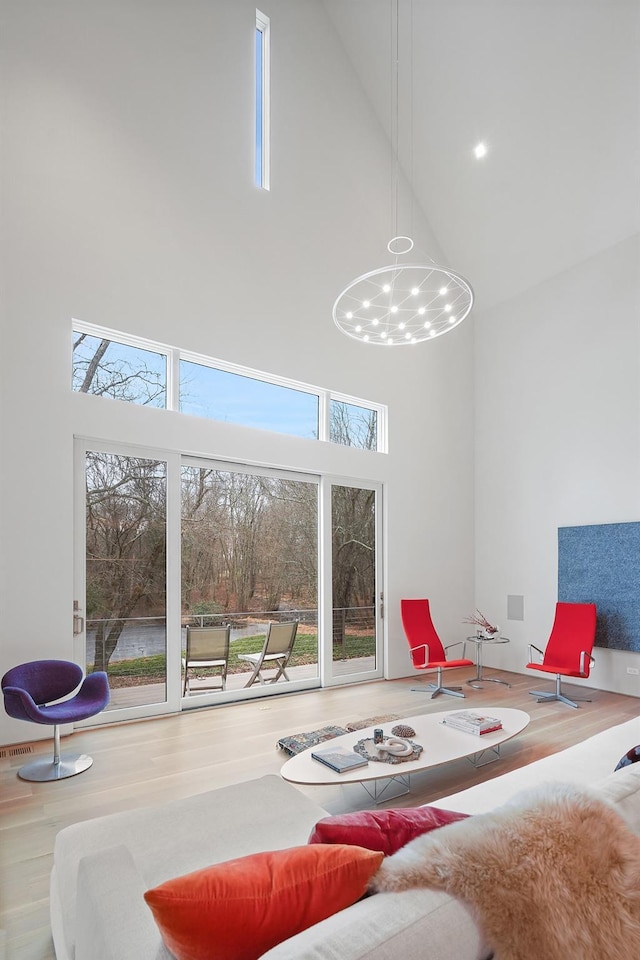 living room featuring hardwood / wood-style floors, a towering ceiling, a healthy amount of sunlight, and an inviting chandelier