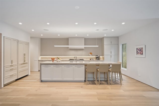 kitchen with a breakfast bar, sink, an island with sink, and light hardwood / wood-style flooring