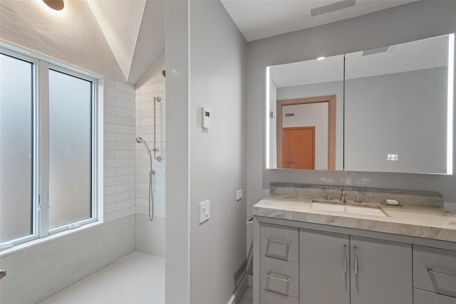 bathroom with vanity, lofted ceiling, tiled shower, and a wealth of natural light