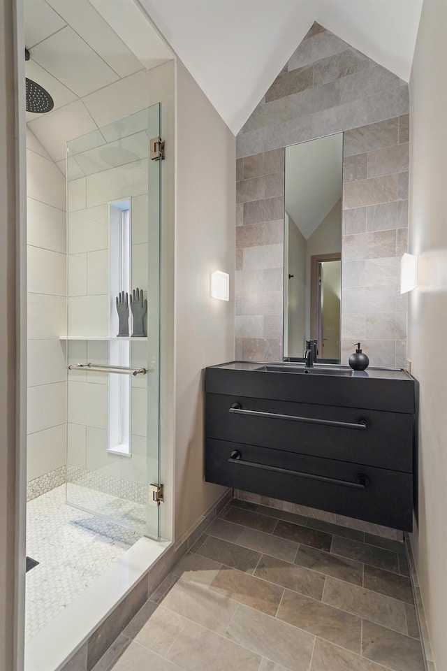 bathroom featuring vanity, a shower with door, vaulted ceiling, and tile walls