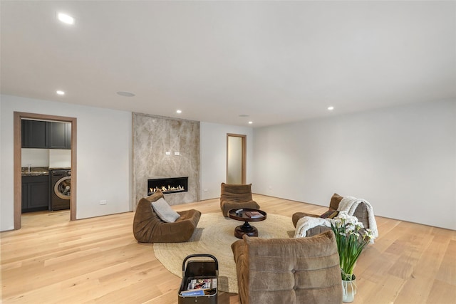 living room with washing machine and clothes dryer, sink, a high end fireplace, and light hardwood / wood-style floors