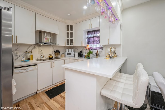 kitchen featuring a kitchen breakfast bar, kitchen peninsula, white cabinetry, and white appliances