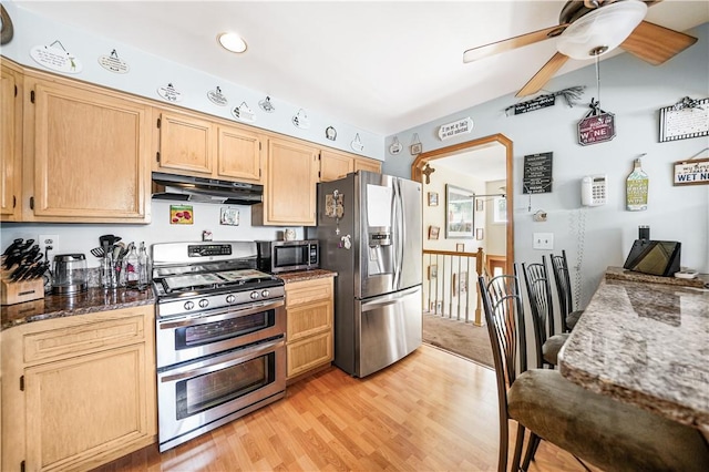 kitchen with light brown cabinets, light wood-type flooring, dark stone countertops, and appliances with stainless steel finishes