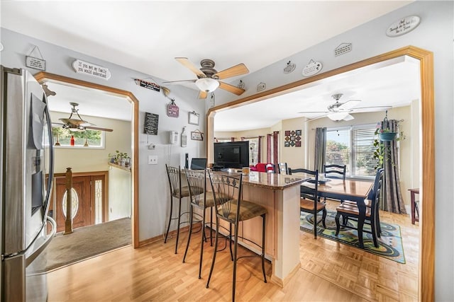 kitchen with a kitchen bar, stainless steel fridge, kitchen peninsula, and ceiling fan