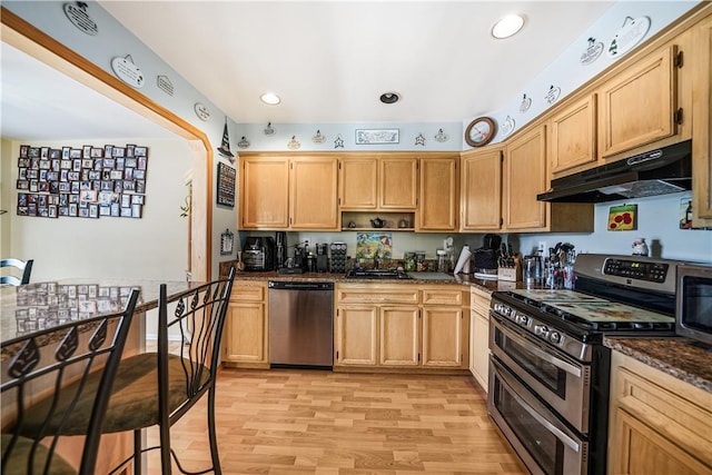 kitchen with appliances with stainless steel finishes, light brown cabinets, dark stone counters, sink, and light wood-type flooring