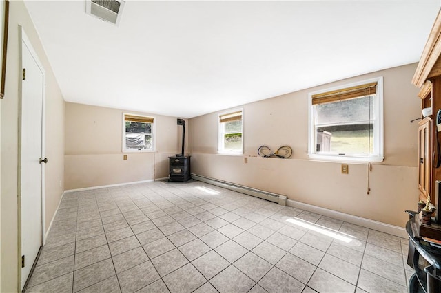 empty room featuring a baseboard radiator, a wood stove, and light tile patterned flooring